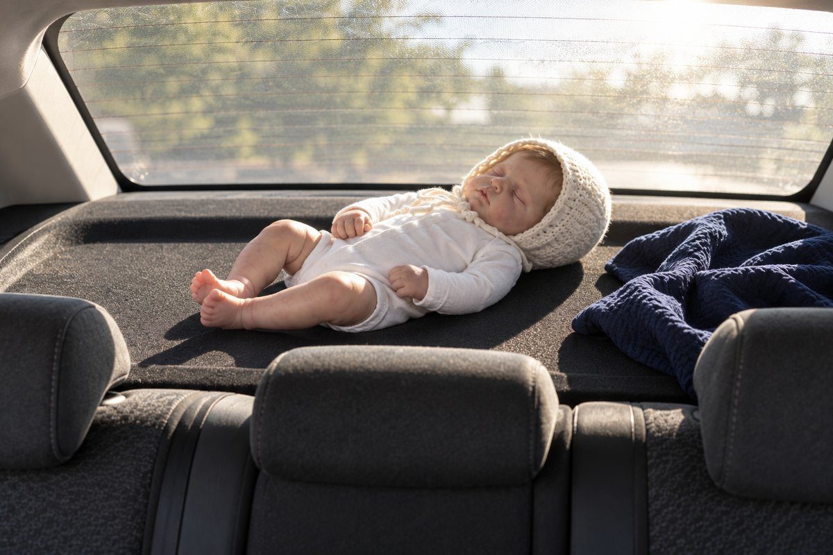 Poupée reborn posée sur la plage arrière d'une voiture en plein soleil